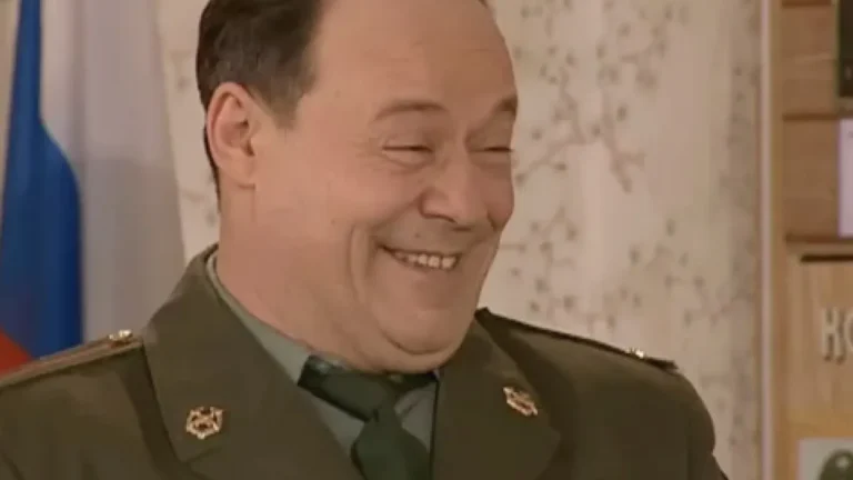 Алексей Маклаков в военной форме улыбается в помещении на фоне флага России и стены с декором — nicetry.blog