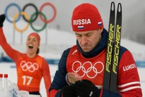 Российский лыжник с опущенной головой стоит на фоне олимпийских колец — рядом спортсменка празднует победу — зимняя трасса и спортивный инвентарь — nicetry.blog
